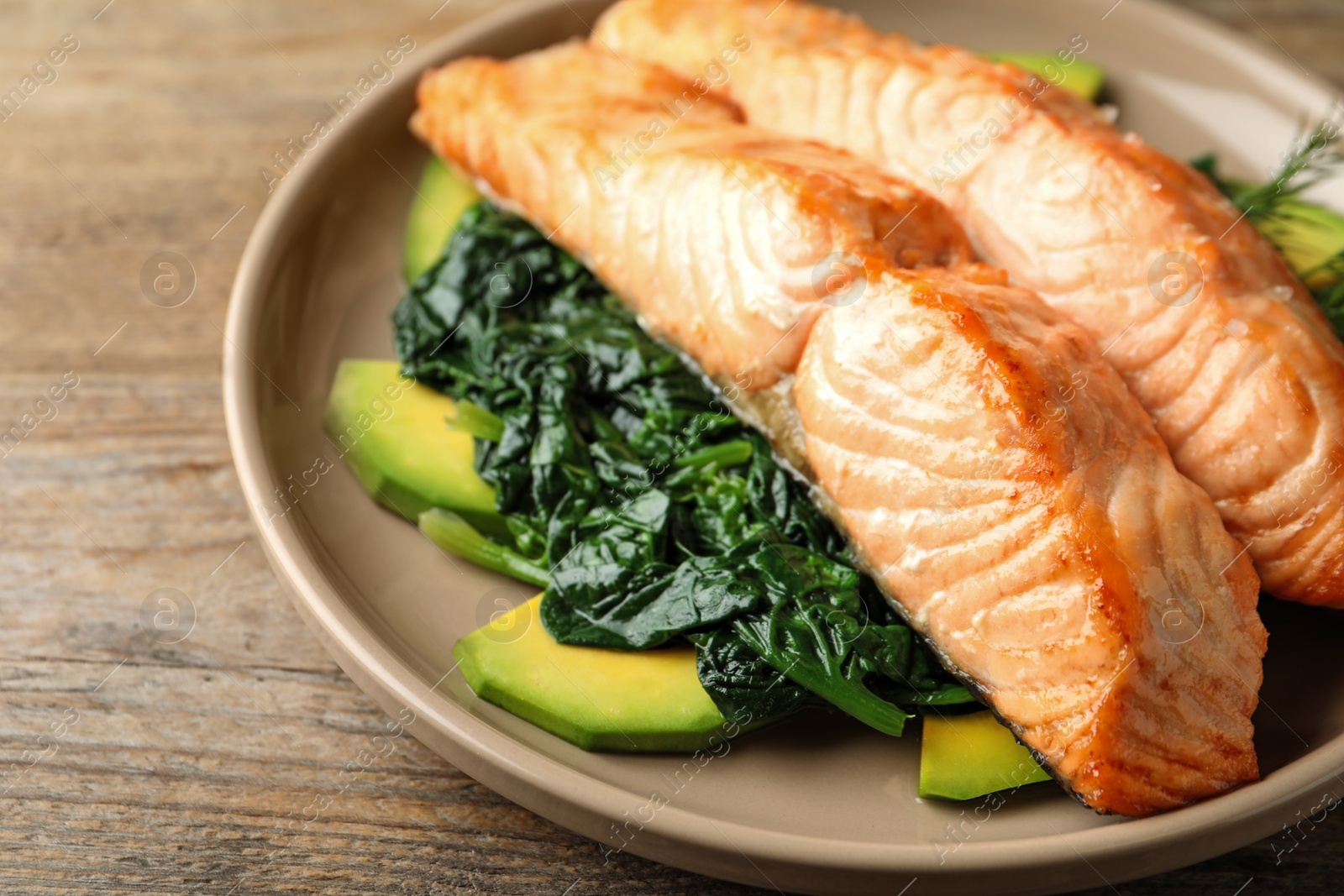 Photo of Tasty salmon with spinach and avocado on wooden table, closeup