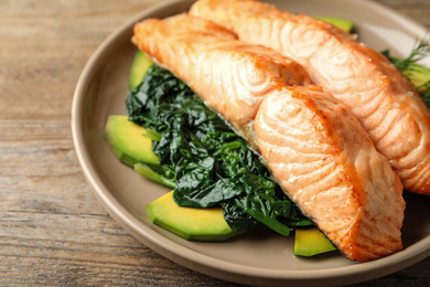 Photo of Tasty salmon with spinach and avocado on wooden table, closeup