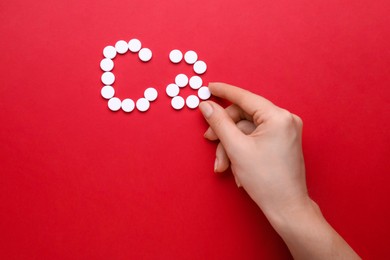 Woman making calcium symbol with white pills on red background, top view