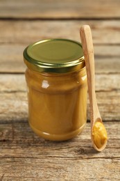 Photo of Jar and spoon with tasty mustard sauce on wooden table, closeup