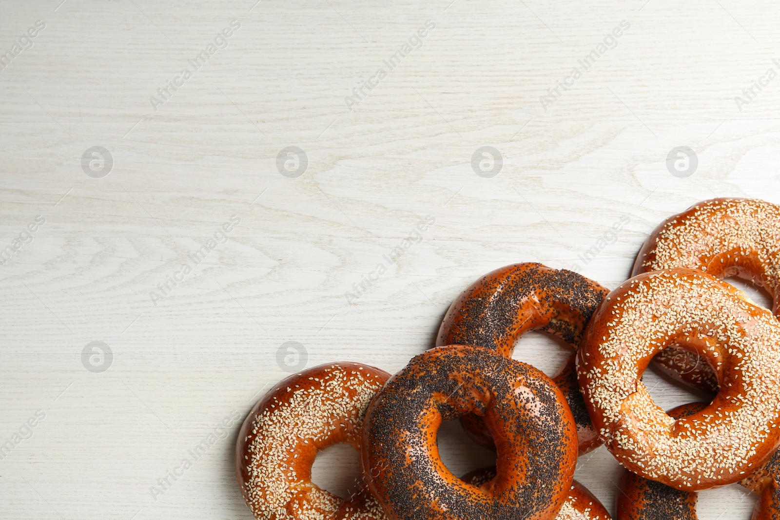 Photo of Many delicious fresh bagels on white wooden table, flat lay. Space for text