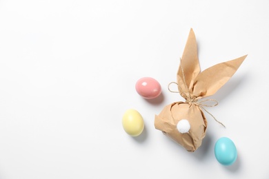 Photo of Easter bunny gift bag and dyed eggs on white background, top view