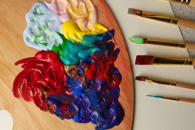 Photo of Artist's palette with mixed bright paints and brushes on textured table, flat lay