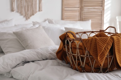 Photo of Basket with warm knitted plaid on bed indoors