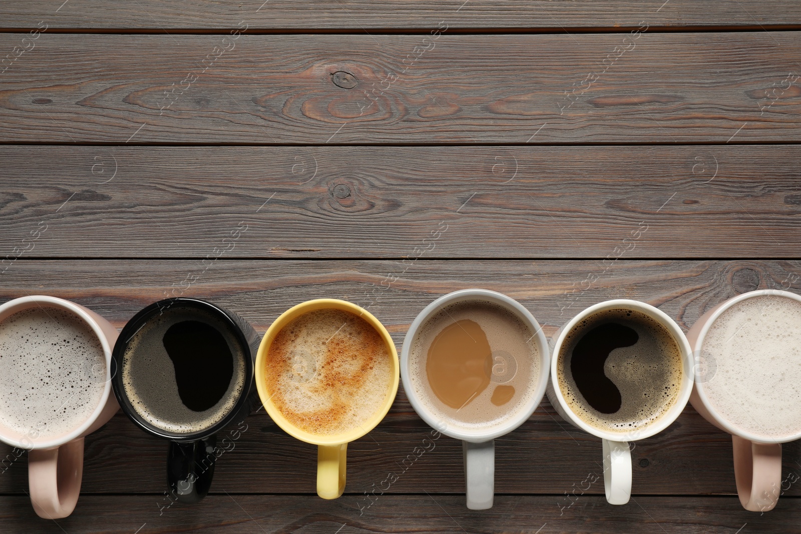 Photo of Many different cups with aromatic coffee on wooden table, flat lay. Space for text