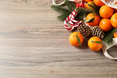 Photo of Fresh tangerines, Christmas candy canes, fir tree branches and cones on wooden table, flat lay. Space for text