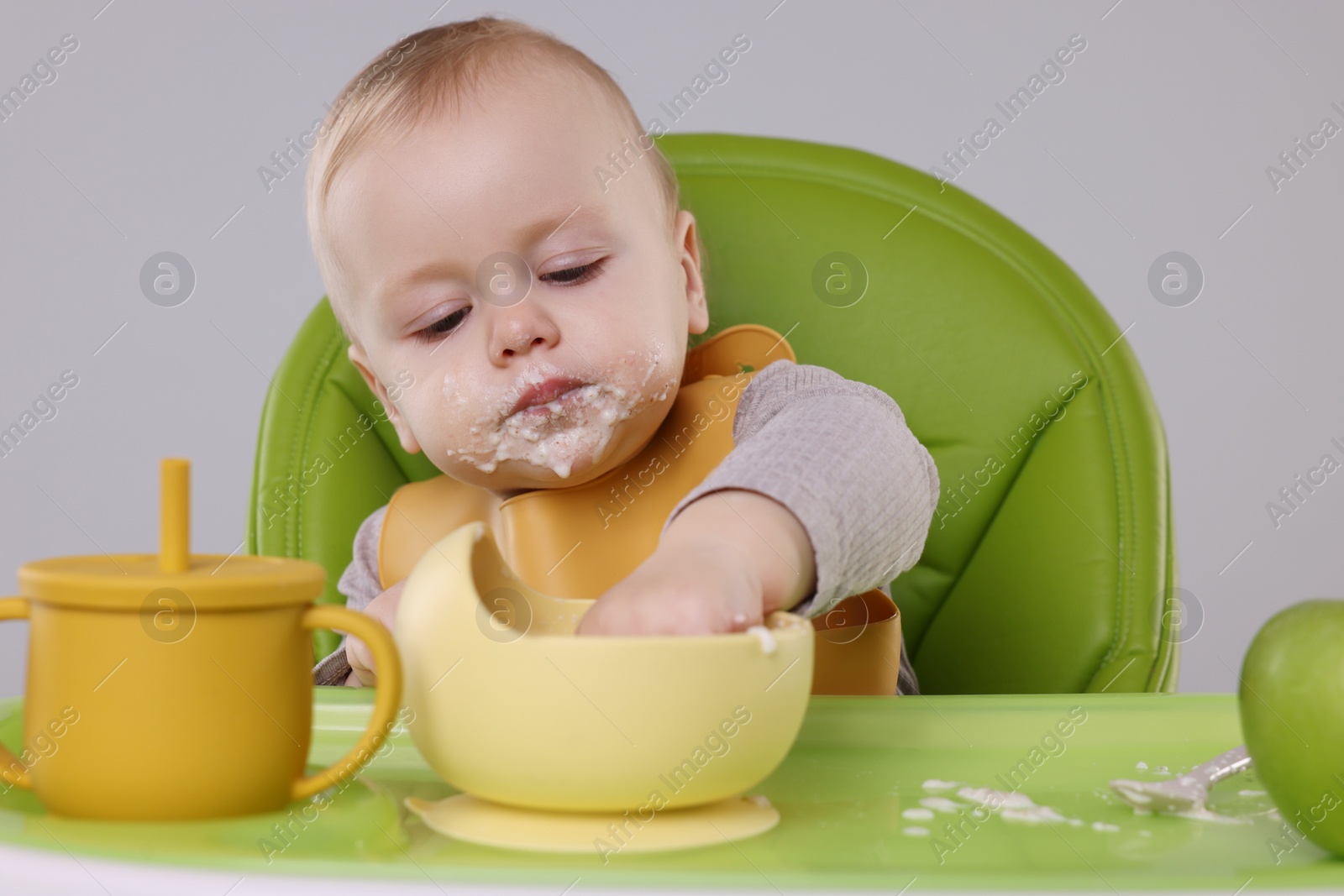 Photo of Cute little baby eating healthy food in high chair on gray background