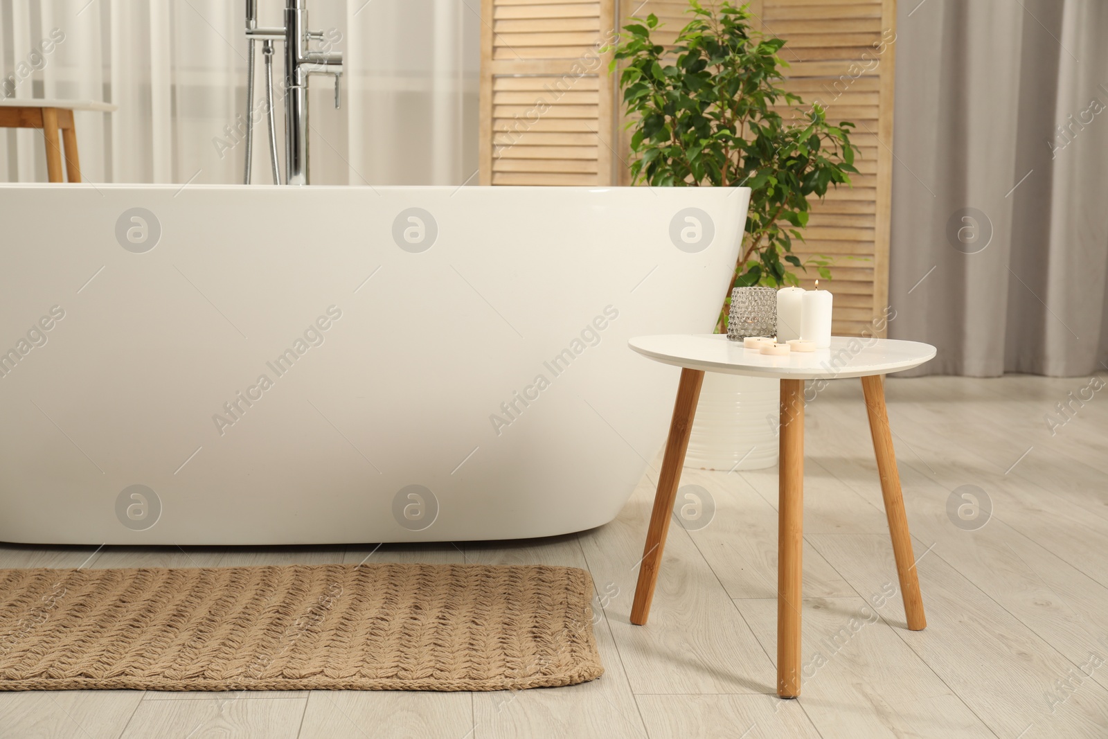 Photo of Spa day. Stylish bathroom with ceramic tub, houseplant and wooden side table