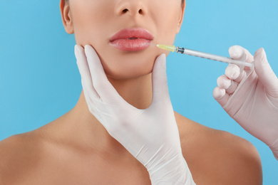 Photo of Woman getting lip injection on light blue background, closeup