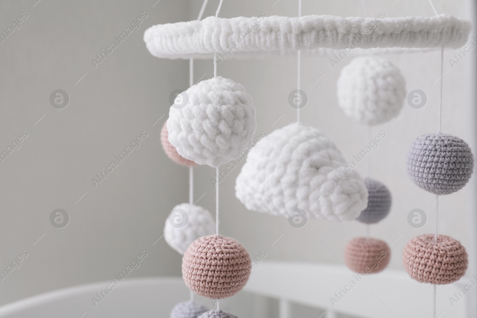 Photo of Modern baby crib mobile near beige wall in room, closeup