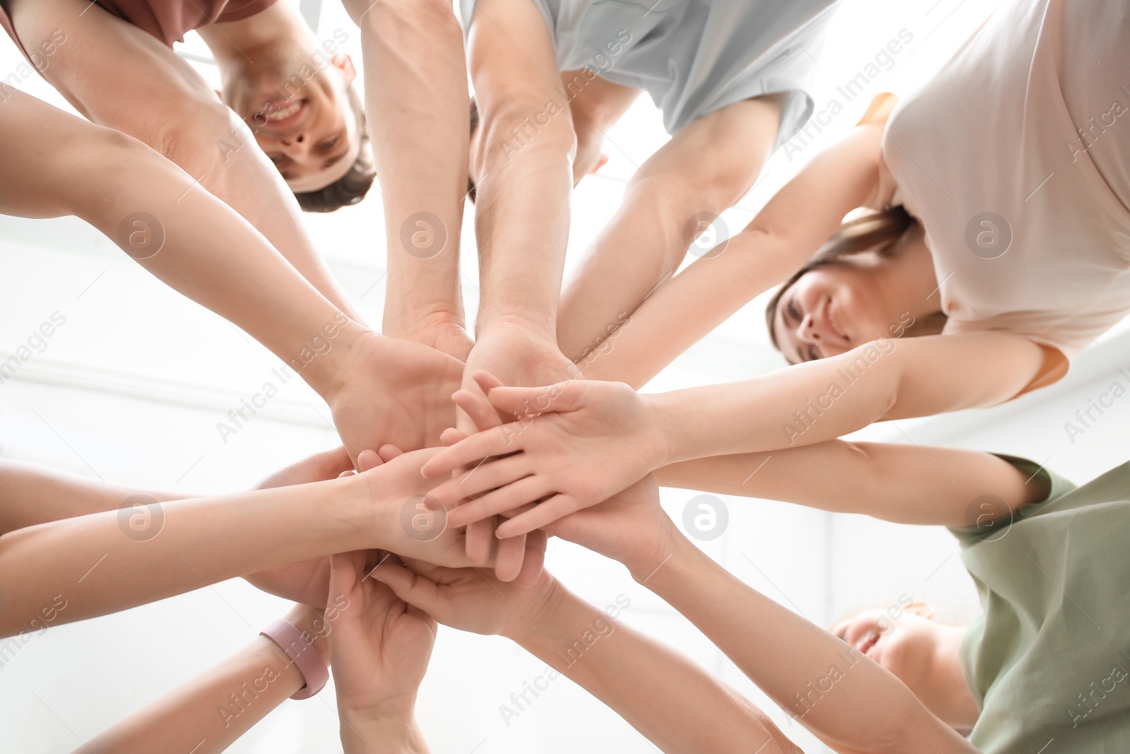 Photo of People putting hands together on light background, closeup. Unity concept
