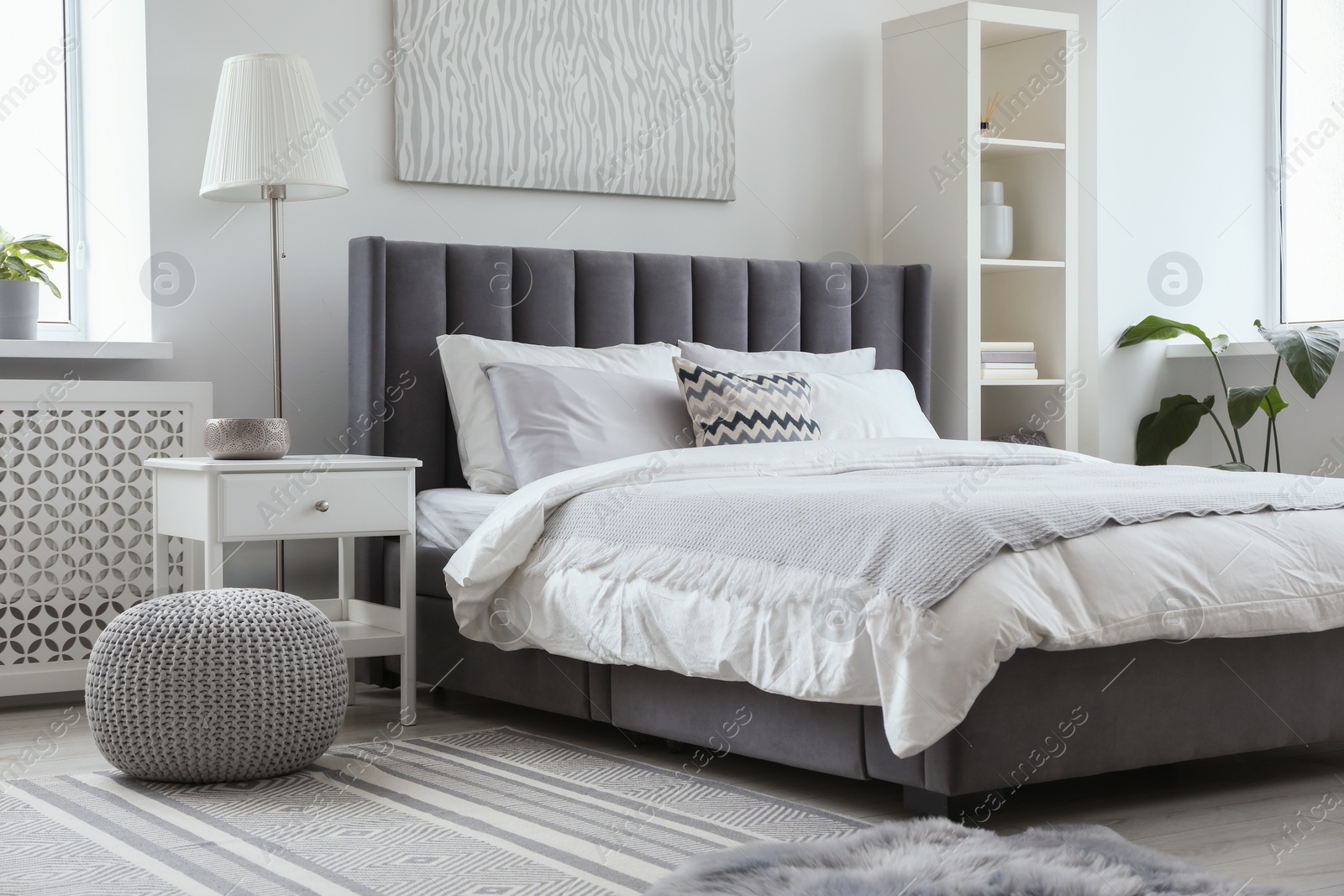 Photo of Stylish light bedroom interior with large comfortable bed, shelving unit and bedside table