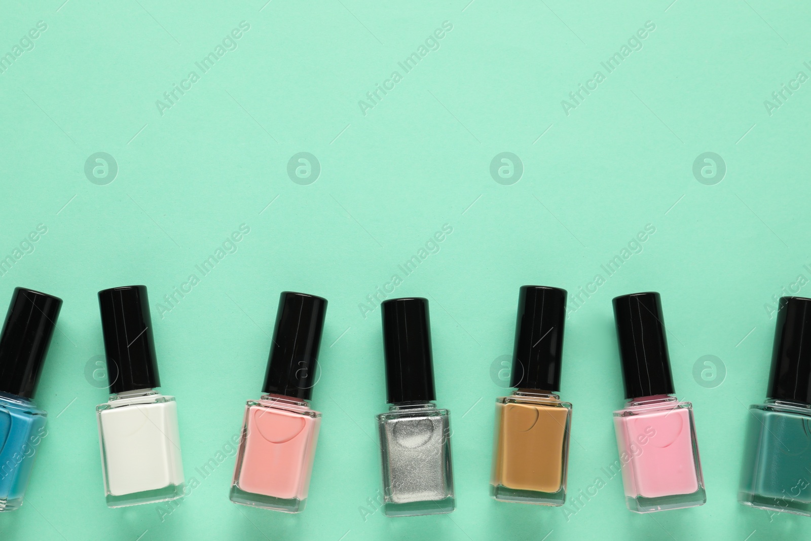 Photo of Bright nail polishes in bottles on turquoise background, flat lay. Space for text