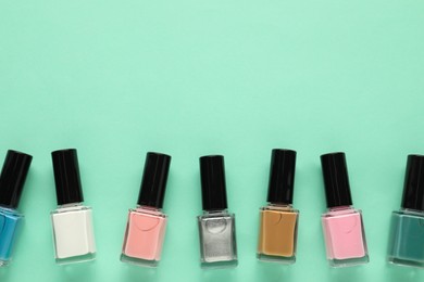 Bright nail polishes in bottles on turquoise background, flat lay. Space for text