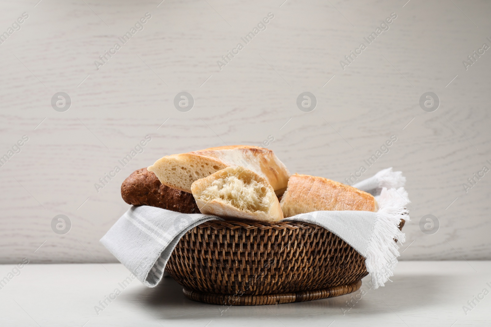 Photo of Different tasty baguettes in basket on white wooden table