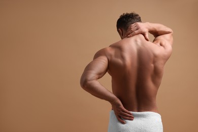 Photo of Man suffering from back and neck pain on beige background, back view. Space for text