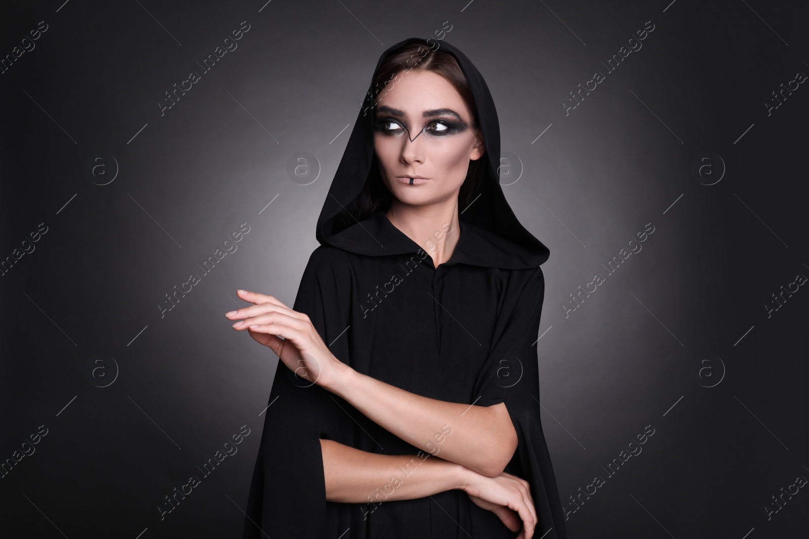 Photo of Mysterious witch in mantle with hood on dark background