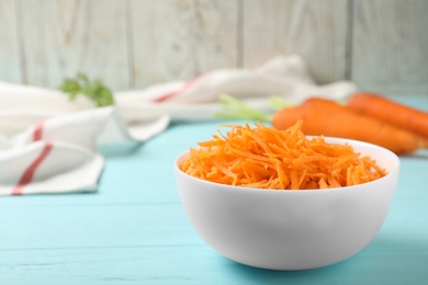 Photo of Bowl of grated carrot on color wooden table. Space for text