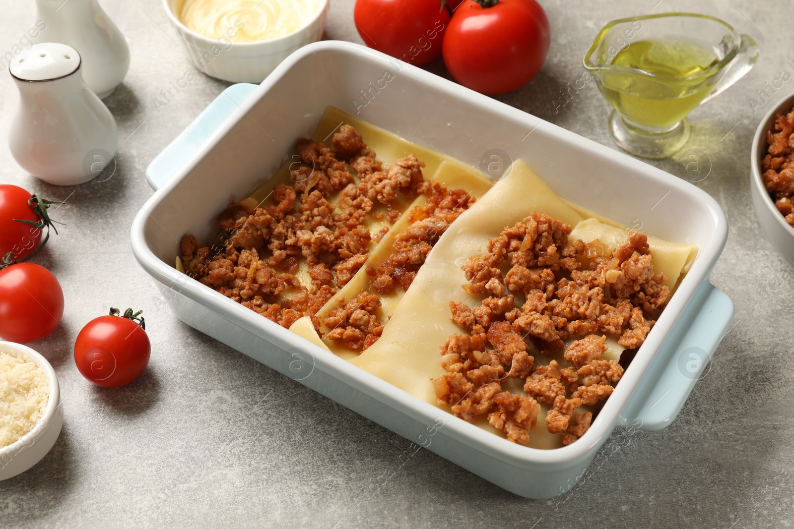 Photo of Cooking lasagna. Pasta sheets and minced meat in baking tray on light textured table