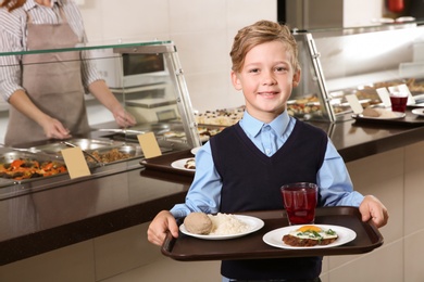 Cute boy holding tray with healthy food in school canteen