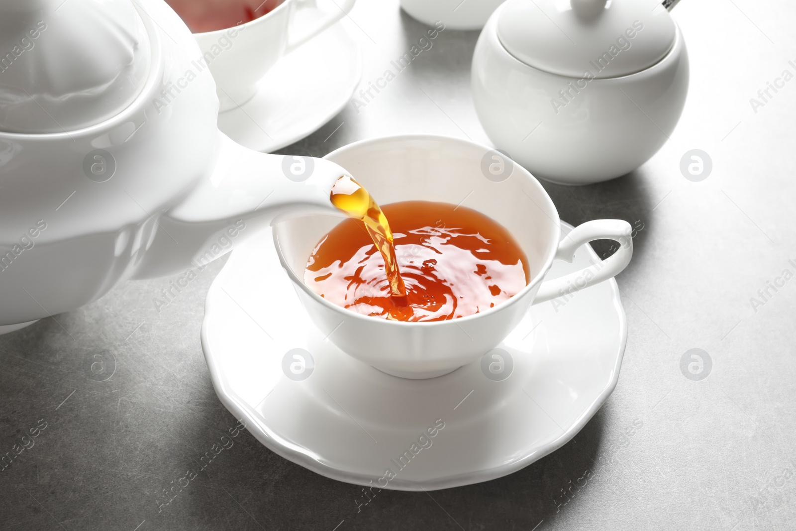 Photo of Pouring hot tea into porcelain cup on table