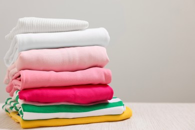 Photo of Stack of folded clothes on wooden table against grey background, space for text