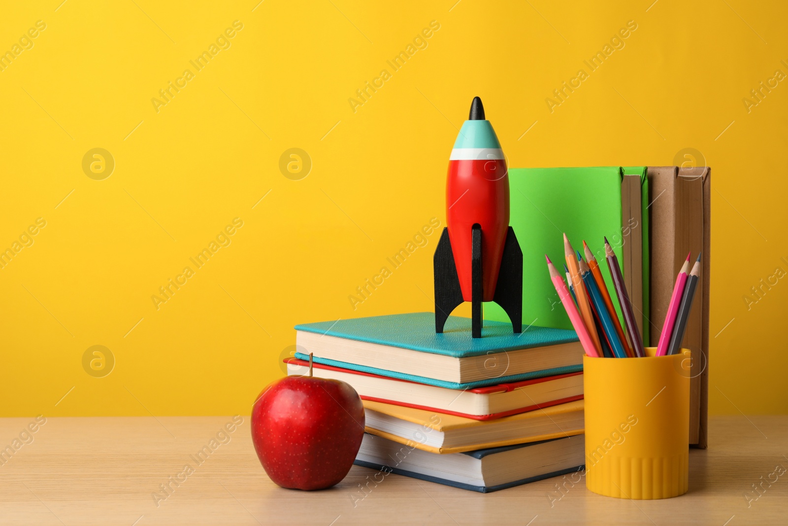 Photo of Bright toy rocket and school supplies on wooden table. Space for text