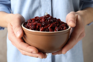 Photo of Woman holding bowl with tasty cranberries on color background, closeup. Dried fruits as healthy snack