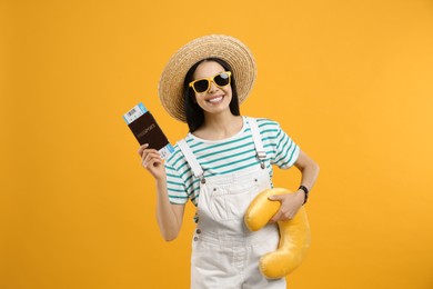 Photo of Happy female tourist with ticket, passport and travel pillow on yellow background