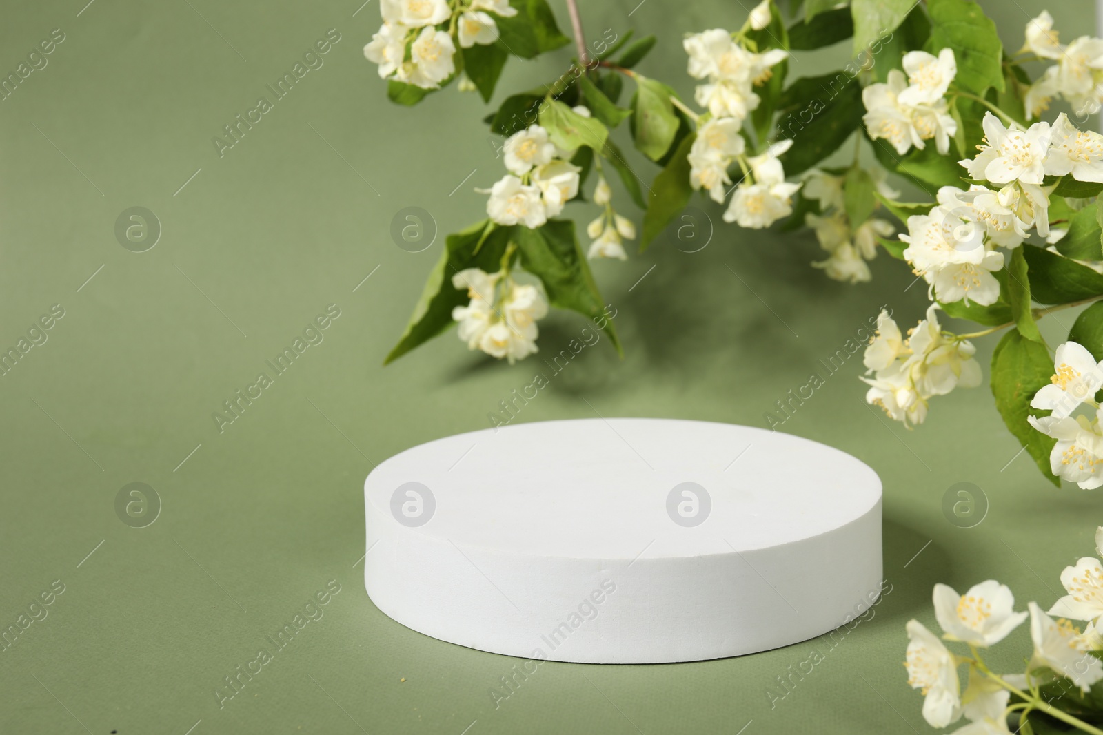 Photo of Presentation of product. White podium among beautiful jasmine flowers on pale green background, space for text