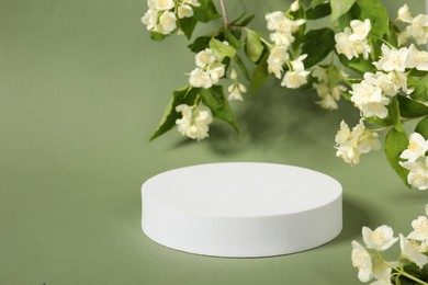 Photo of Presentation of product. White podium among beautiful jasmine flowers on pale green background, space for text