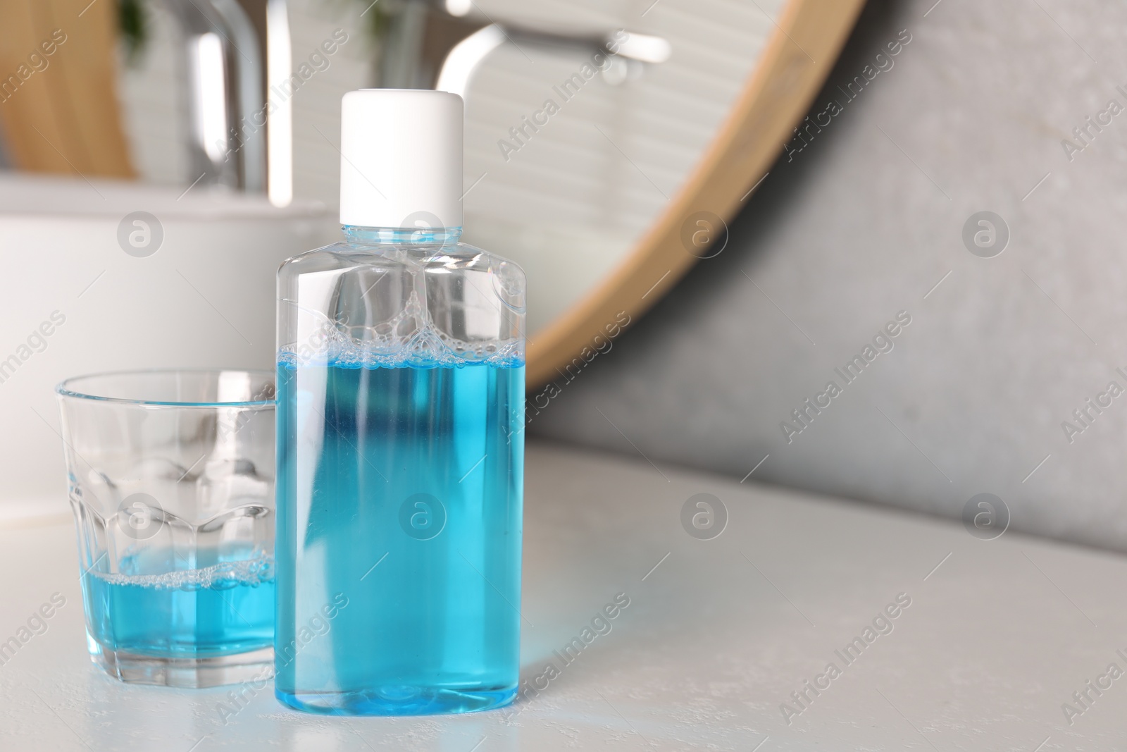 Photo of Bottle and glass of mouthwash on white countertop in bathroom, space for text