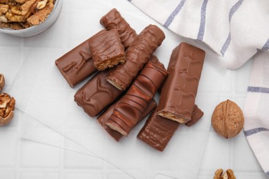 Different tasty chocolate bars and walnuts on white tiled table, flat lay
