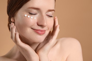 Photo of Beautiful woman with freckles and cream on her face against beige background, closeup