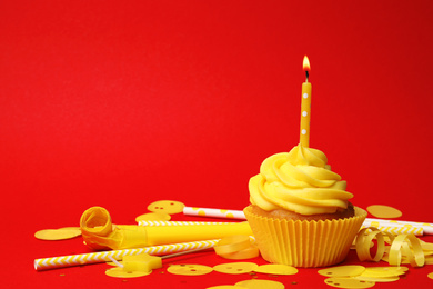 Delicious birthday cupcake with yellow cream and burning candle on red background. Space for text