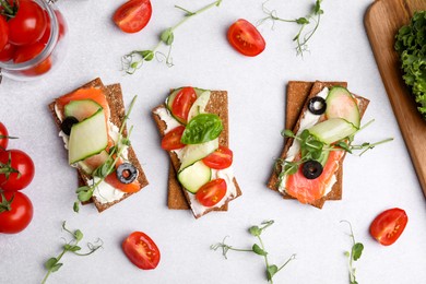 Photo of Tasty rye crispbreads with salmon, cream cheese and vegetables on light grey table, flat lay