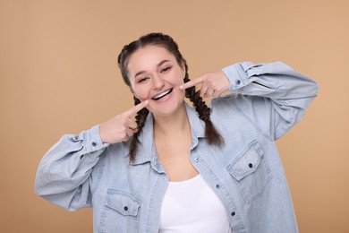Happy woman pointing at braces on her teeth against beige background