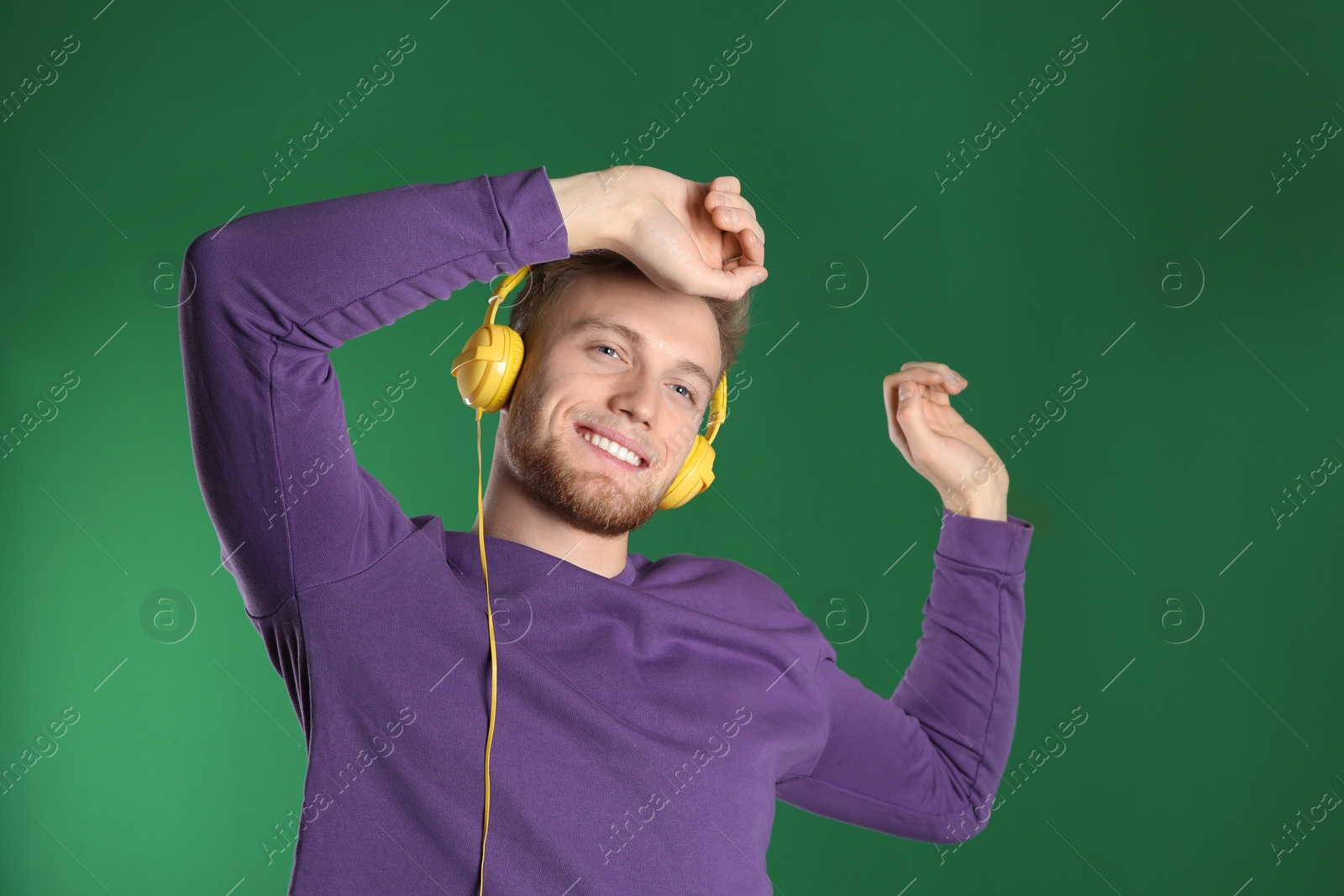 Photo of Handsome young man listening to music with headphones on color background