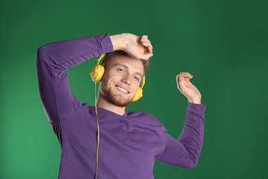 Photo of Handsome young man listening to music with headphones on color background