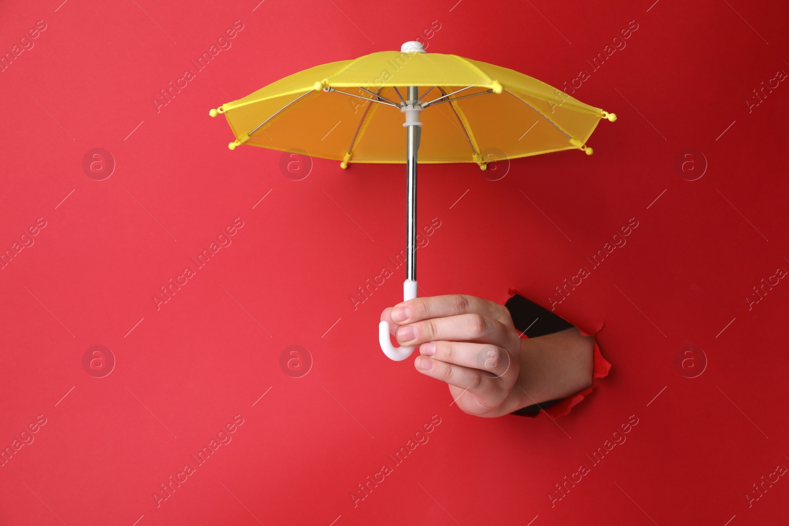 Photo of Woman holding open small yellow umbrella through hole in red paper, closeup