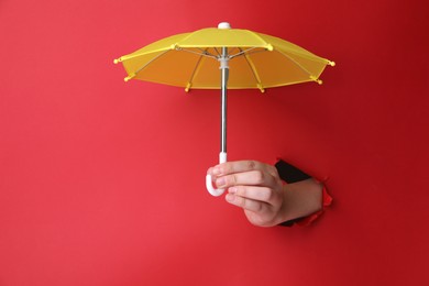 Photo of Woman holding open small yellow umbrella through hole in red paper, closeup
