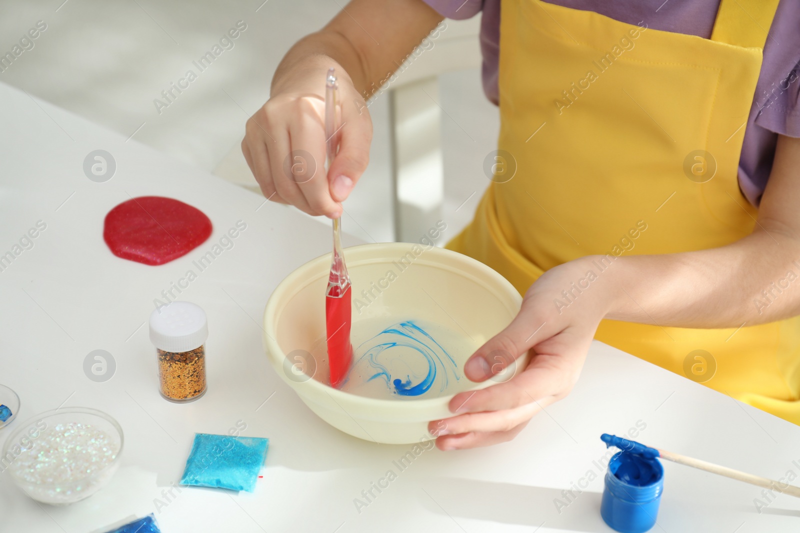 Photo of Little girl mixing ingredients with silicone spatula at table, closeup. DIY slime toy