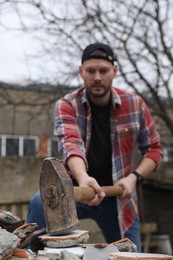 Photo of Man breaking bricks with sledgehammer outdoors, selective focus