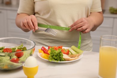 Photo of Overweight woman measuring waist while having meal at home, closeup