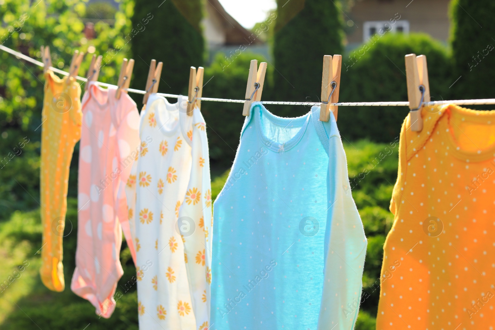 Photo of Clean baby onesies hanging on washing line in garden. Drying clothes