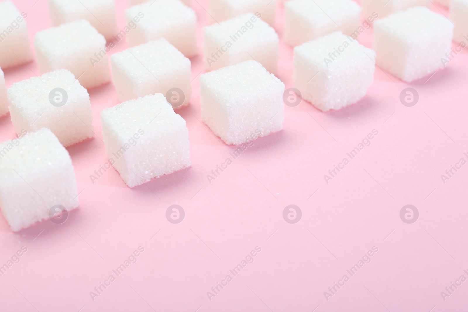 Photo of White sugar cubes on pink background, closeup. Space for text