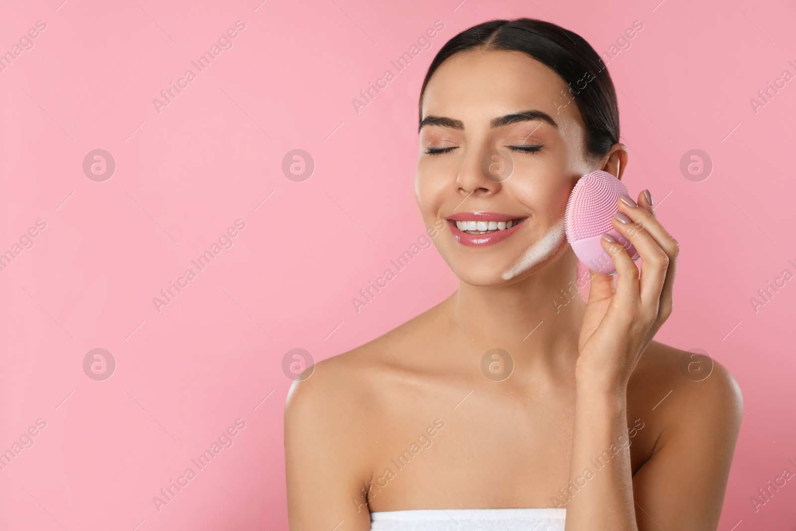 Photo of Young woman using facial cleansing brush on pink background, space for text. Washing accessory