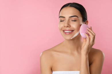 Photo of Young woman using facial cleansing brush on pink background, space for text. Washing accessory