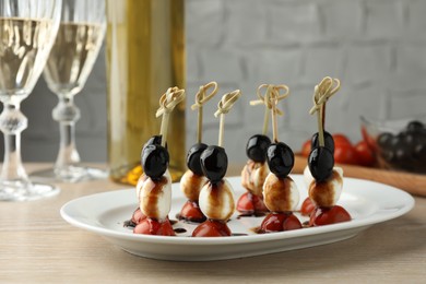 Tasty canapes with black olives, mozzarella and cherry tomatoes on light wooden table, closeup