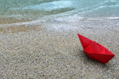 Beautiful red paper boat on sandy beach near water outdoors, space for text